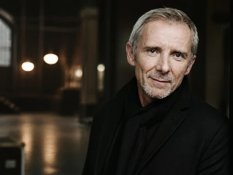 Portrait de l'acteur Geoffroy Thiébaut portant un manteau noir dans un décor intérieur sombre et élégant