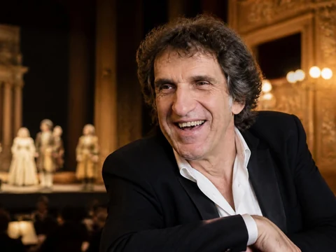 Gilles Benizio sourit devant la scène d'un opéra où des comédiens sont en représentation