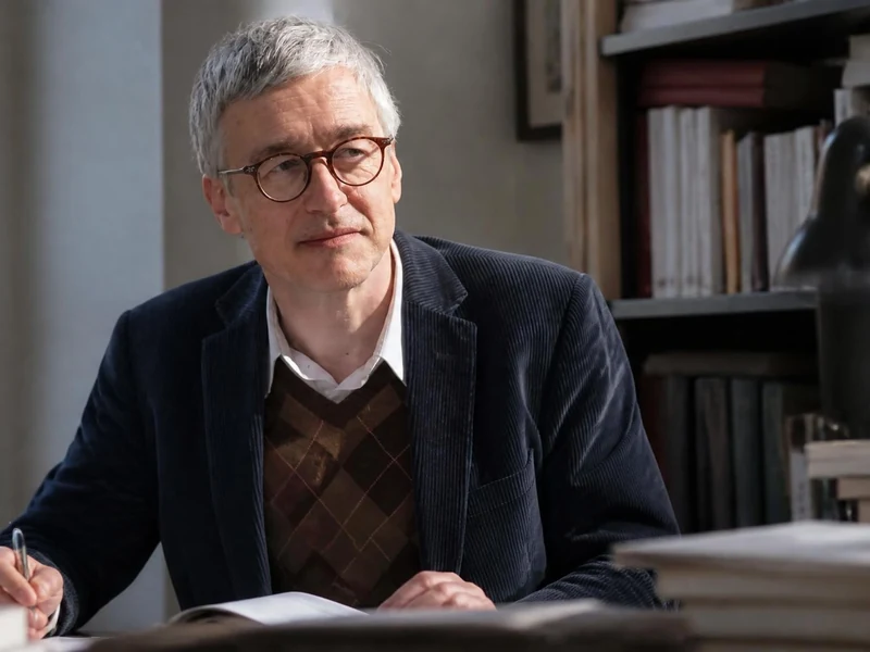 Portrait de l'éditeur Hugues Jallon assis à son bureau devant une bibliothèque remplie de livres