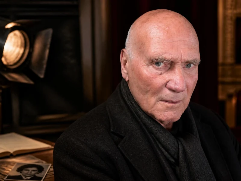 Portrait de l'acteur Jean-Paul Zehnacker posant dans un décor de théâtre sombre éclairé par un projecteur