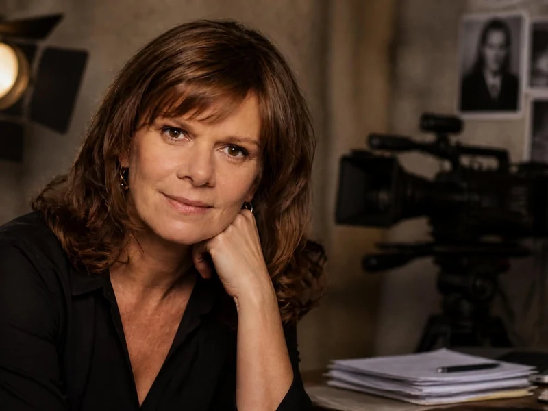 Portrait de Laure Duthilleul posant dans un studio de tournage avec une caméra en arrière-plan