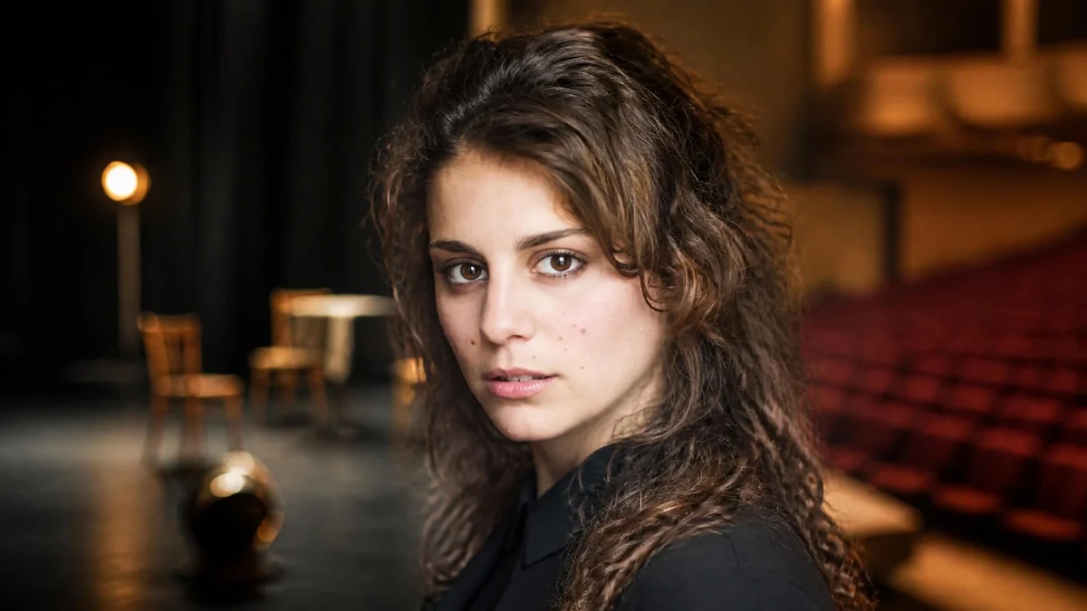 Portrait de la comédienne Lou Chauvain posant sur une scène de théâtre sombre