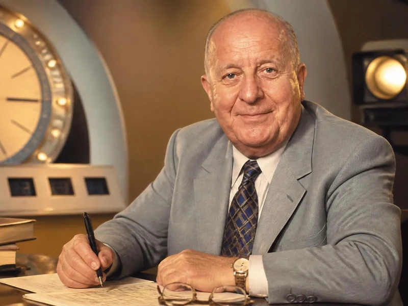 Portrait de Max Favalelli assis à son bureau devant une horloge de jeu télévisé