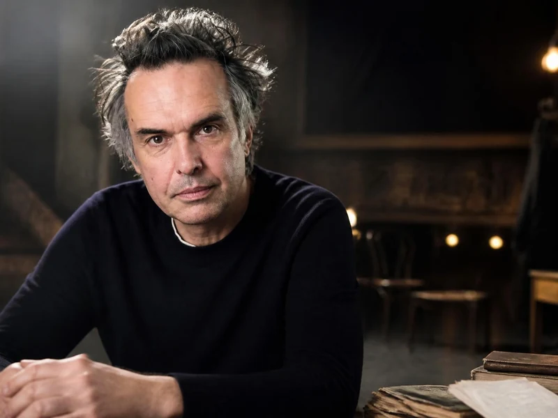 Portrait de l'acteur Nicolas Bouchaud posant avec sérieux dans un décor de théâtre sombre et épuré