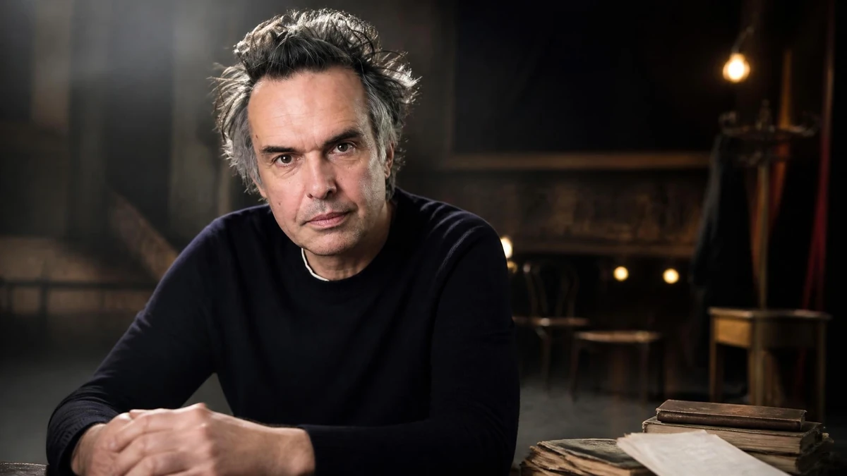 Portrait de l'acteur Nicolas Bouchaud posant avec sérieux dans un décor de théâtre sombre et épuré
