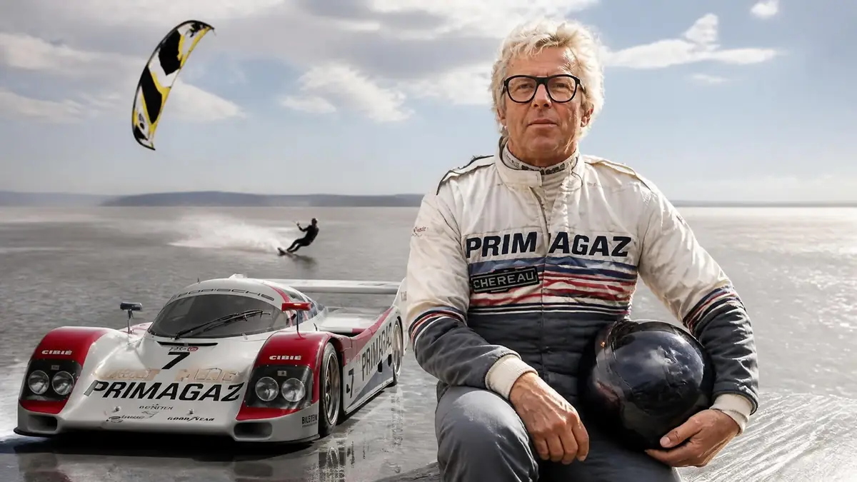 Le pilote Pierre Yver pose avec son casque devant une voiture de course sur une étendue d'eau avec un kitesurfeur en fond