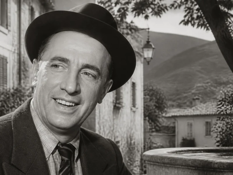 Portrait en noir et blanc de l'acteur français Rellys souriant devant une fontaine de village