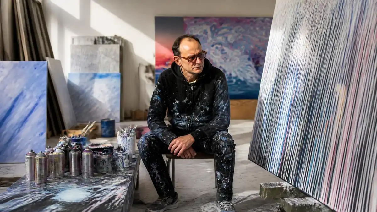 L'artiste tanc est assis dans son atelier entouré de ses toiles abstraites et de bombes de peinture