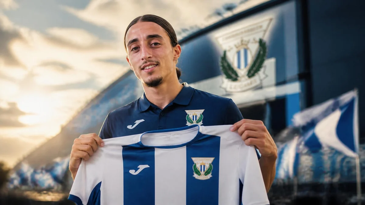 Le footballeur Yassine Kechta présente fièrement un maillot de son club devant un stade en arrière-plan